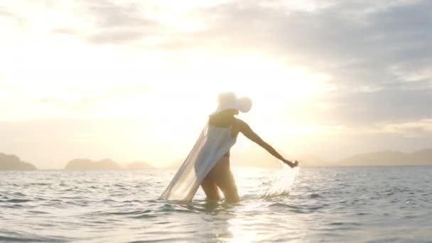 Vrouw in string spetteren water in zee naar gloeiende zonsondergang — Stockvideo