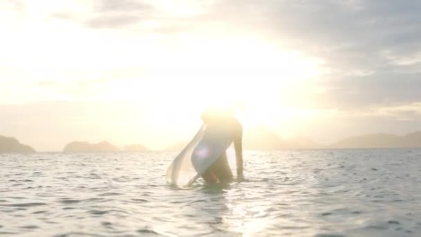 Kobieta w stringach struganie wody w morzu w kierunku świecącego zachodu słońca — Wideo stockowe