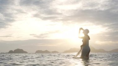 Bikinili Kadın ve Güneş Batarken Denizde Duran Güneş Şapkalı Kadın