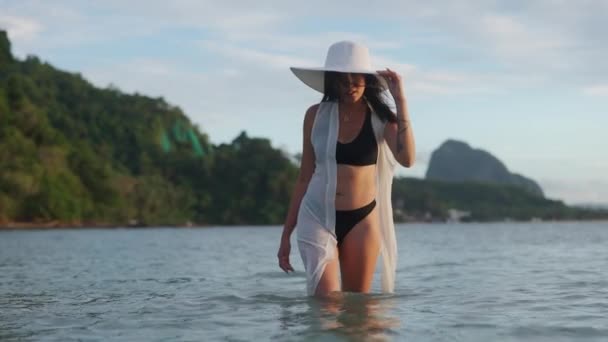 Vrouw in bikini en zonnehoed wandelen in zee — Stockvideo
