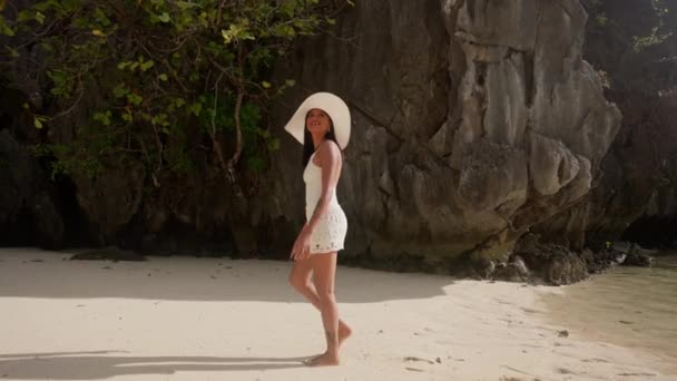 Женщина в шапке и шортах, идущая по скрытому пляжу — стоковое видео