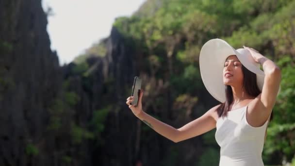 Женщина улыбается в солнечной шляпе, чтобы позировать для селфи на смартфоне — стоковое видео