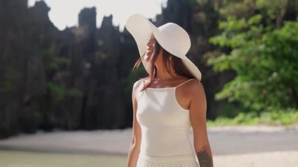 Glimlachende vrouw met zonnehoed die langs het verborgen strand loopt — Stockvideo