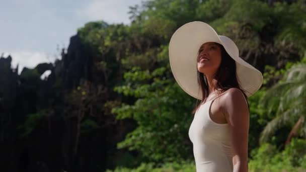 Glimlachende vrouw met zonnehoed die langs het verborgen strand loopt — Stockvideo