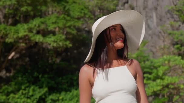 Glimlachende vrouw met zonnehoed die langs het verborgen strand loopt — Stockvideo