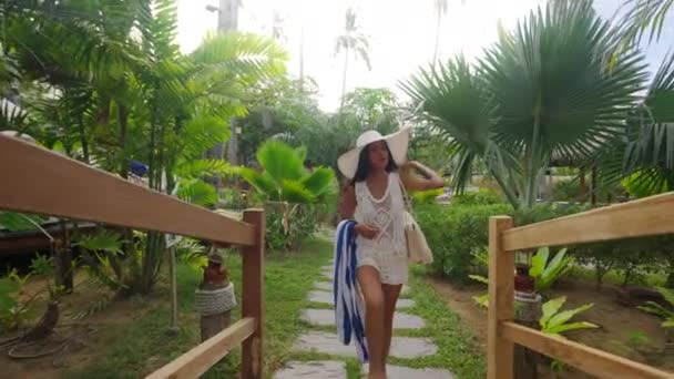 Kobieta w kapeluszu spaceruje z ręcznikiem plażowym przez kładkę — Wideo stockowe