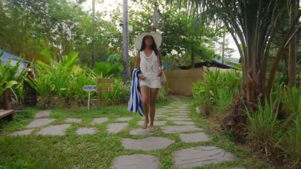 Жінка у сонячному капелюсі йде з пляжним рушником на зворотному шляху — стокове відео