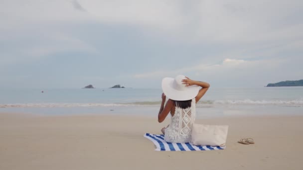 Woman In Sunhat Sitting On Beach Towel Looking Out To Sea — Stock video