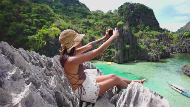 Женщина сидит на известняковых скалах и фотографируется со смартфоном — стоковое видео