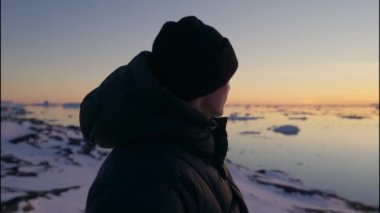 Ilulissat Icefjord, Grönland 'da gün batımına bakan Sıcak Giysili Adam' ın Yavaş Çekim Çekimi