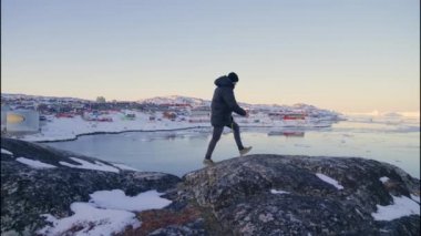 Ilulissat Icefjord, Grönland sahilinden görüntüye bakmak için Kayalıklarda Yürüyen Sıcak Giysili Adam 'ın Yavaş Çekimi