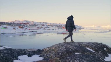 Ilulissat Icefjord, Grönland sahilinden görüntüye bakmak için Kayalıklarda Yürüyen Sıcak Giysili Adam 'ın Yavaş Çekimi