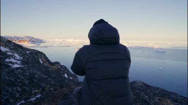 格陵兰岛Ilulissat Icefjord海岸线岩石上的相机三脚架对穿着暖和衣服的人的中等慢动作射击 — 图库视频影像
