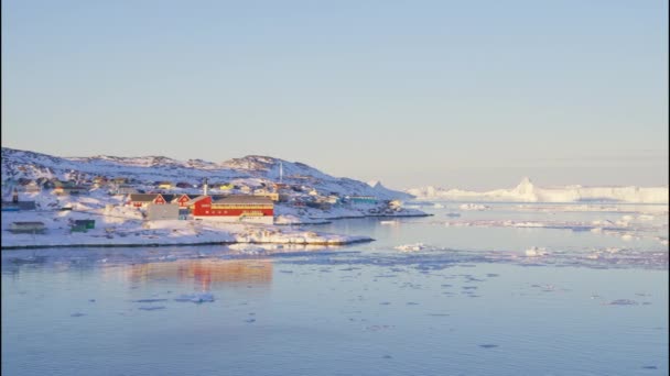 グリーンランド イルリサットの氷と海へと向かう海岸線の陽光が降りそそぐ町からの広いスローモーション パンニング ショット — ストック動画