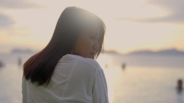 Gün batımına karşı koyu saçlı güzel bir Asyalı kadının portresi. Yan tarafa bakıyor ve gülümsüyor. Sakin atmosfer. Yavaş Hareket Görüntüsü