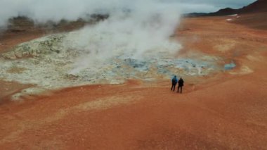 Myvatn Gölü yakınlarındaki Hver Jeotermal Bölgesi 'nde Buharlı Fümerollere Bakan İki Turistin Hava Çekimi. Geniş açılı panoramik çekim. Kamera İleriye Taşır