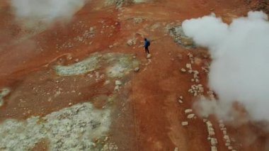 Myvatn Gölü 'nün yakınlarındaki Hver Jeotermal Bölgesi' nde bulunan Dumanlı Fumaroleler üzerinde. İzlanda. Geniş açılı panoramik çekim. Drone Buharın Üzerinde Uçuyor. Erkek Turist İleri Yürür. Yüksek Açı Atışı