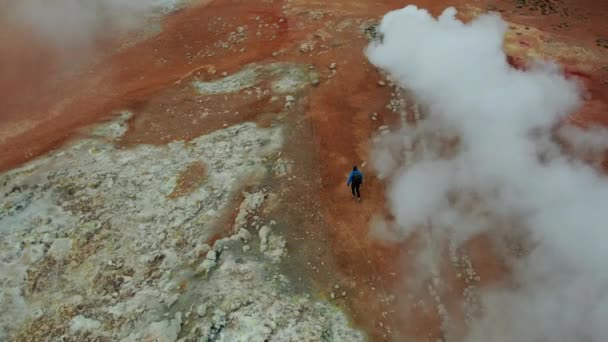 Myvatn湖の近くのHverir地熱地域の蒸しフマロールの上空 アイスランド パノラマワイドショット ドローンは蒸気の上を飛ぶ 男の観光客が前に歩く 高角度ショット — ストック動画