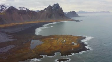 İzlanda fiyortlarının üzerinde havadan. Deniz kıyısındaki kar örtülü dağların nefes kesici manzarası. Geniş açılı panoramik çekim. Kamera Sola Taşır