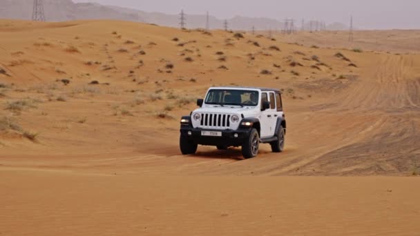 ドバイの砂漠を運転する男と白いジープの広いスローモーション追跡ショット — ストック動画