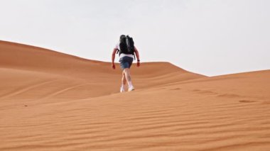 Sırt çantalı bir adamın Dubai 'deki kum tepecikleri üzerinde yürürken çekilmiş ağır çekim görüntüleri.