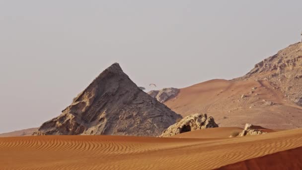 ドバイ砂漠での岩の形成の背後にパラグライダー人のワイドスローモーションロックダウンショット — ストック動画