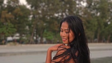 Gün batımında, Tayland 'da genç ve güzel bir kadının kumsalda kameraya dönüşmesini gösteren yavaş çekim.