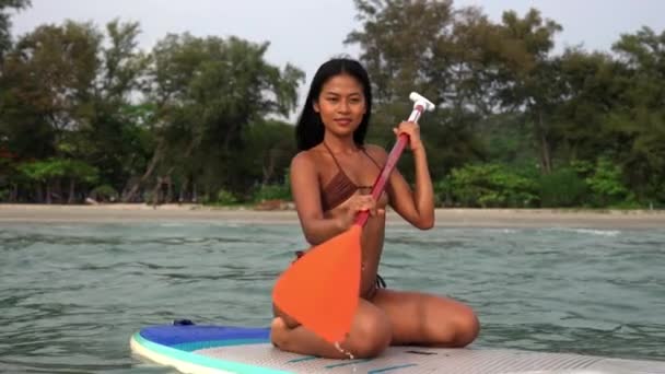 タイの海でパイドルボードを編み 漕いでいるビキニの若い女性の笑顔の幅広いスローモーションショットを追跡 — ストック動画