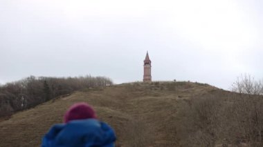 Tourist with Backpack Enjoys View of the Red Brick Tower on Top of Himmelbjerget Hill, Denmark. Focus Is on the Background. Bottom Up Shot. Camera Zooms Out