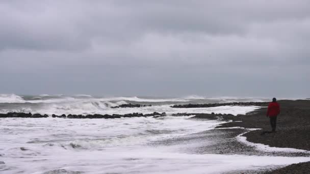 Człowiek Zimowych Ciuchach Spaceruje Nad Morzem Skalistym Wybrzeżu Ogląda Nadchodzącą — Wideo stockowe