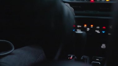 Close-up Shot of Drivers Hand Is on the Gear Transmission Box. Dashboard Lights On. View From the Back Seat of a Car. Shallow Focus