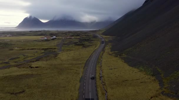 冰岛一条空旷的沿海公路上行驶的汽车的空中 高山与峡湾之间的路与被覆盖的天空相映成趣 令人惊叹的风景 全景宽射门 — 图库视频影像