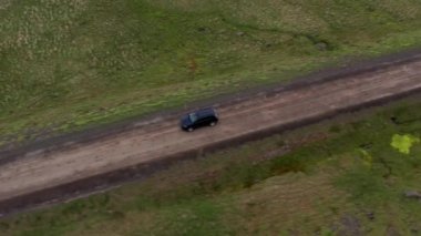 Aerial of a Car Driving Along an Empty Rural Road Between Green Fields In Iceland. Beautiful Landscape. High Angle Tilt Down Shot. Camera Tracking the Car