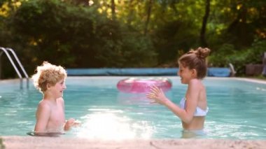 İki Sarı Saçlı Çocuk ve Kızıl Saçlı Kız Birbirlerine Su Sıçratarak Havuzda Eğleniyorlar. Yaz Tatili Konsepti. Yavaş Hareket Görüntüsü