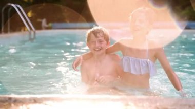 İki Sarı Saçlı Çocuk ve Havuzda Eğlenen Kızıl Saçlı Kız. Önce kameraya bakıyorlar sonra birbirlerine bakıyorlar. Lens üzerindeki fişeklerle Yavaş Hareket Döndürme Görüntüsü