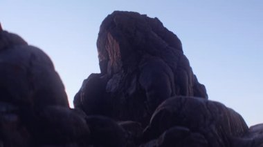 Wide Handheld Arcing Shot Of Rock Formation On Beach Under Blue Sky At Sunset