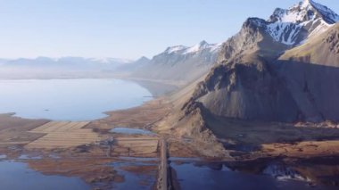 Fiyort ve İzlanda Dağları boyunca uzanan boş bir toprak yolda. Göz kamaştırıcı manzara. Kamera yukarı doğru hareket ediyor. Geniş Panoramik Görüntü