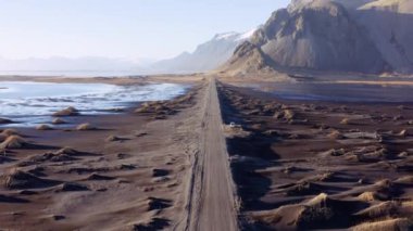 Aerial Over an Empty Dirt Road Along Fjords and Mountains. Stunning Landscape. Drone Takes Off and Rises. Panoramic Wide Shot