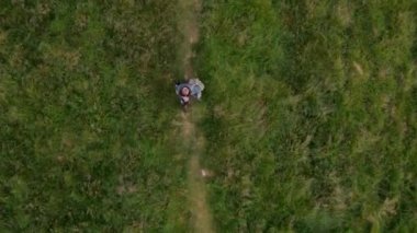 Yeşil çayır boyunca yürüyen ve ellerini kaldıran bir adamın havadan tepeden aşağı görüntüsü. Kamera adamı takip ediyor.