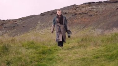 Omzunda çuval olan şık bir adam ve Bulutlu Gökyüzüne Karşı Yeşil Çayırda Yürüyen Banjo Davası. Sinema Ağır Çekim Dolly Out. Kamera Erkeğin Önündedir.