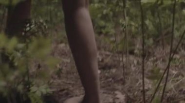 Low Angle Close Up Handheld Tracking Shot Of Barefoot Man And Woman Walking Through Forest