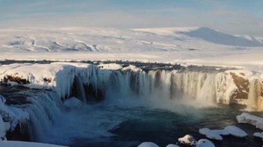 zoom out wide shot of sunlit godafoss waterfall and Skjalfandafljot river with snow and ice, iceland