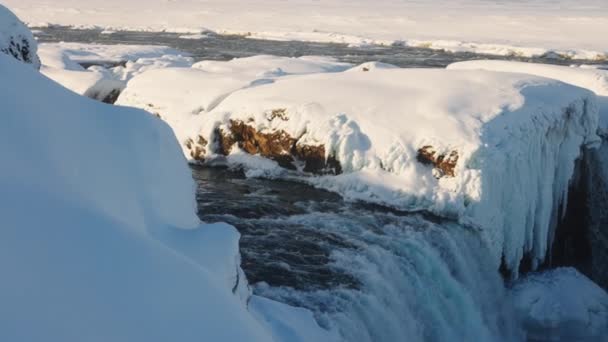wide panning shot of sunlit godafoss waterfall and Skjalfandafljot river with snow and ice, iceland
