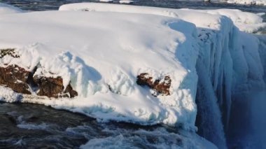 wide slow motion panning shot of sunlit godafoss waterfall and Skjalfandafljot river with snow and ice, iceland