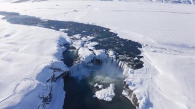 wide drone pulling back over Skjalfandafljot river and godafoss waterfall in snow covered landscape, iceland