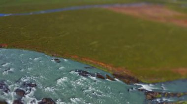 wide tilt shift drone shot pulling back over green landscape surrounding  godafoss waterfall and Skjalfandafljot river, iceland