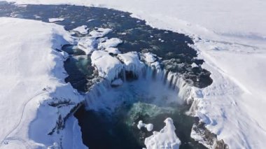 wide drone arcing overhead of Skjalfandafljot river and godafoss waterfall in snow covered landscape, iceland
