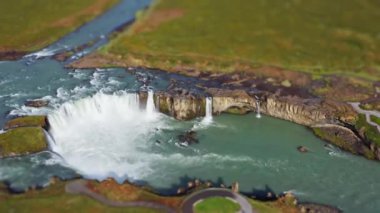 wide tilt shift drone shot panning over green landscape surrounding  godafoss waterfall and Skjalfandafljot river, iceland