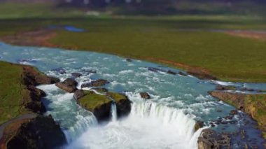 wide tilt shift drone shot zooming in and tilting down over green landscape surrounding  godafoss waterfall and Skjalfandafljot river, iceland