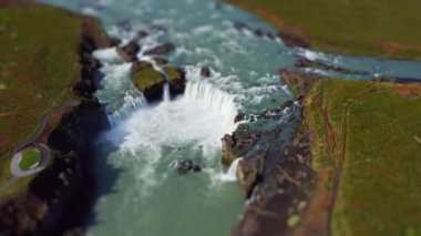 wide tilt shift drone shot panning over green landscape surrounding  godafoss waterfall and Skjalfandafljot river, iceland